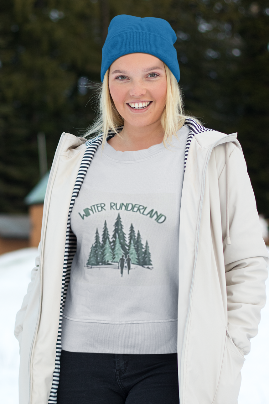 Woman in snowy outdoors wearing a blue hat and an open parka with a shirt that says Winter Runderland with drawn images of pine trees and silhouettes of runners.