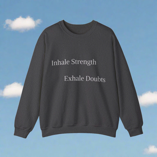 A stylish black sweatshirt with the Inhale Strength Exhale Doubt slogan printed on the front, displayed against a sky background with fluffy white clouds by Printify.