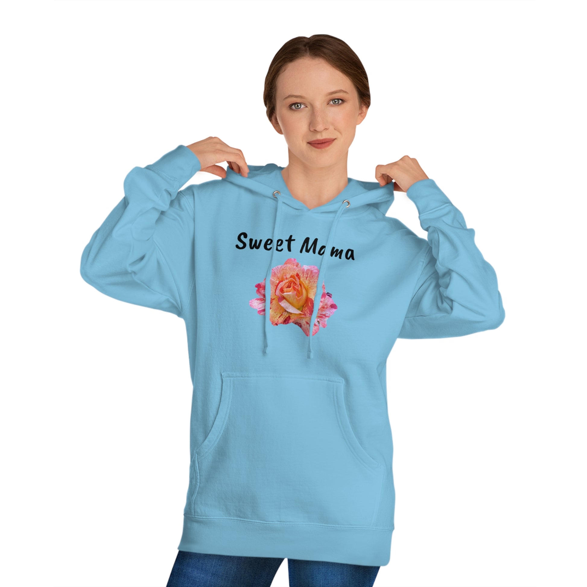 A woman in a Printify Sweet Mama Hooded Sweatshirt light blue hoodie with the phrase "sweet mama" and a pink rose design printed on the front, holding the hood and looking directly at the camera