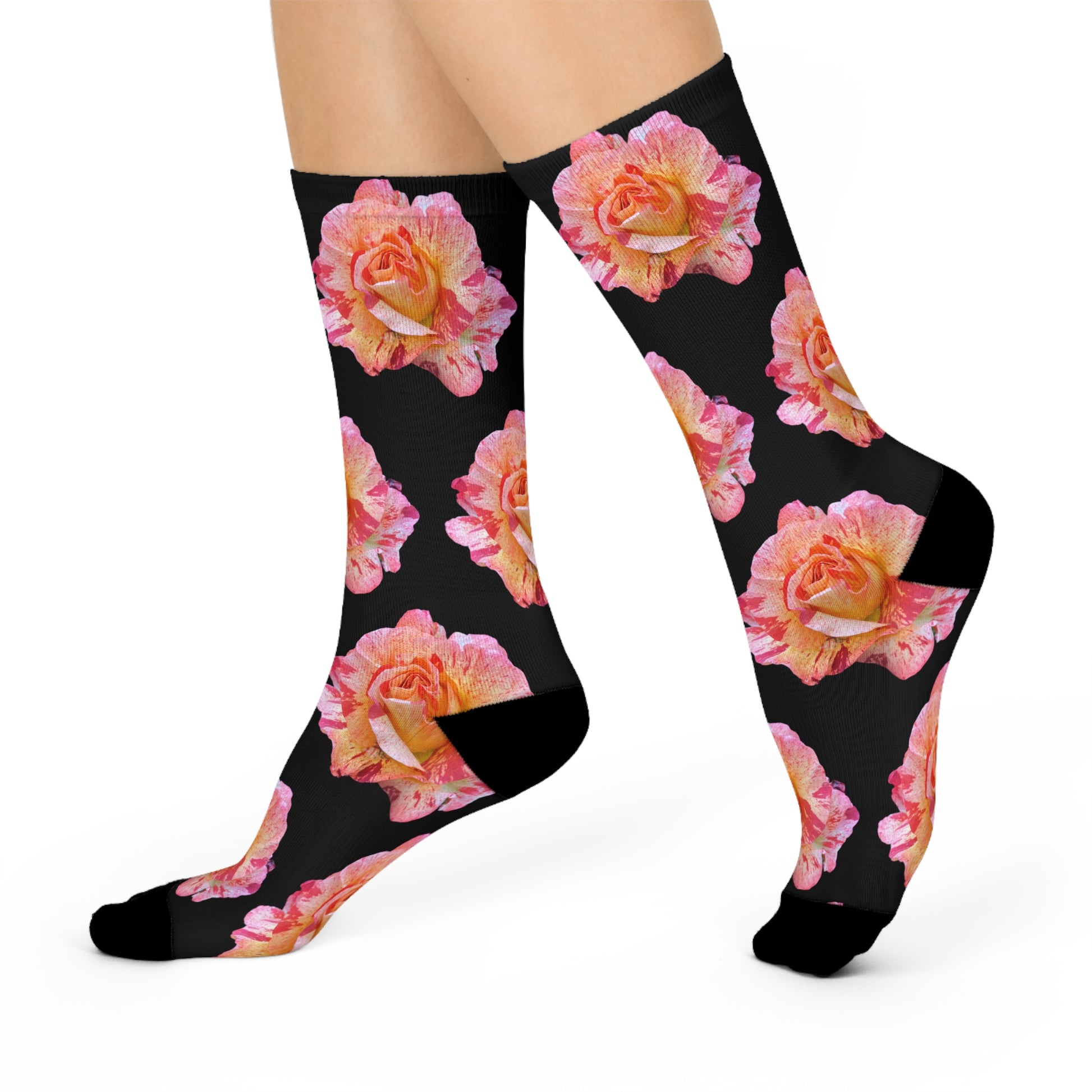 A pair of feet wearing black athletic socks adorned with a vibrant pattern of pink and orange roses against a dark background, presented on a plain white backdrop. The socks are the Roses - Cushioned Crew Socks for Women by Printify.