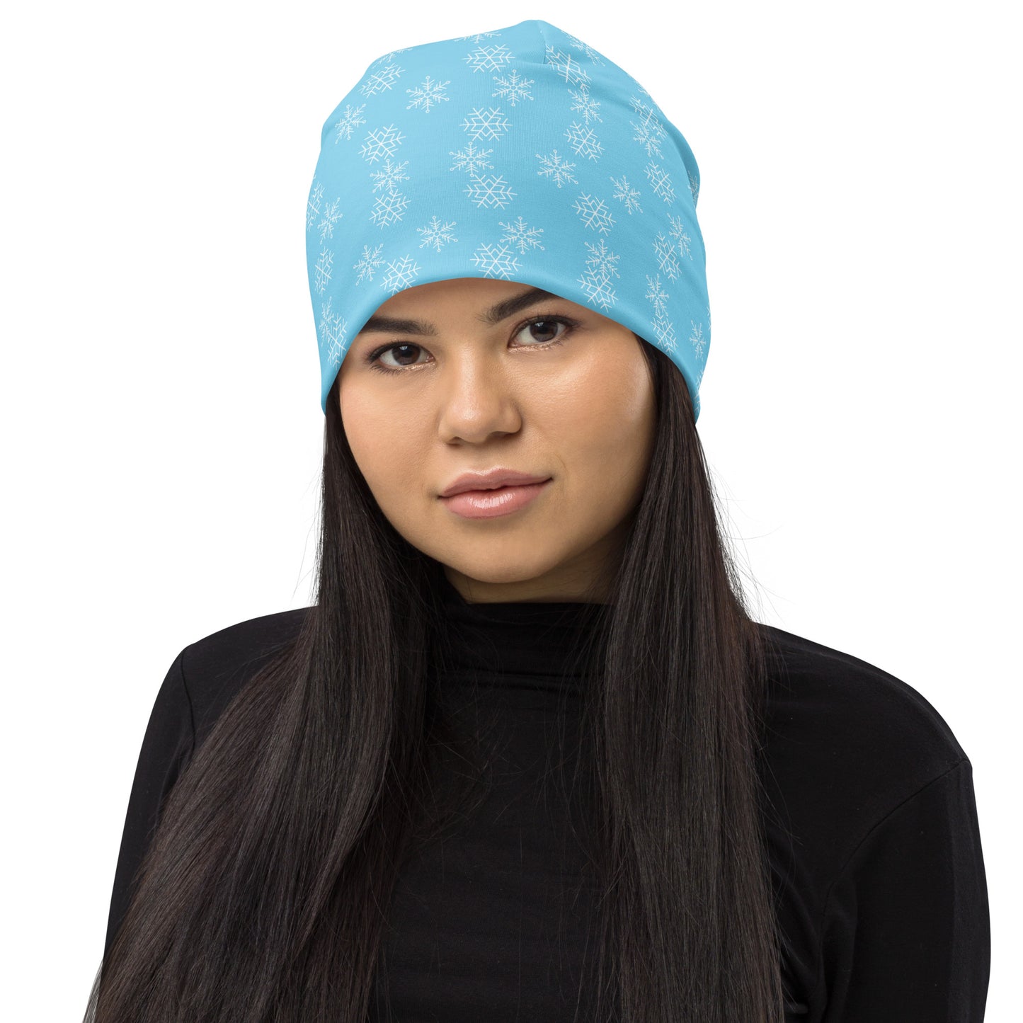 A person with long dark hair wearing a Snowflakes Beanie by Blue Sky Runners, featuring a stylish light blue hue adorned with white snowflakes, paired with a black turtleneck. The double-layered design of the beanie stands out beautifully against the plain white background.