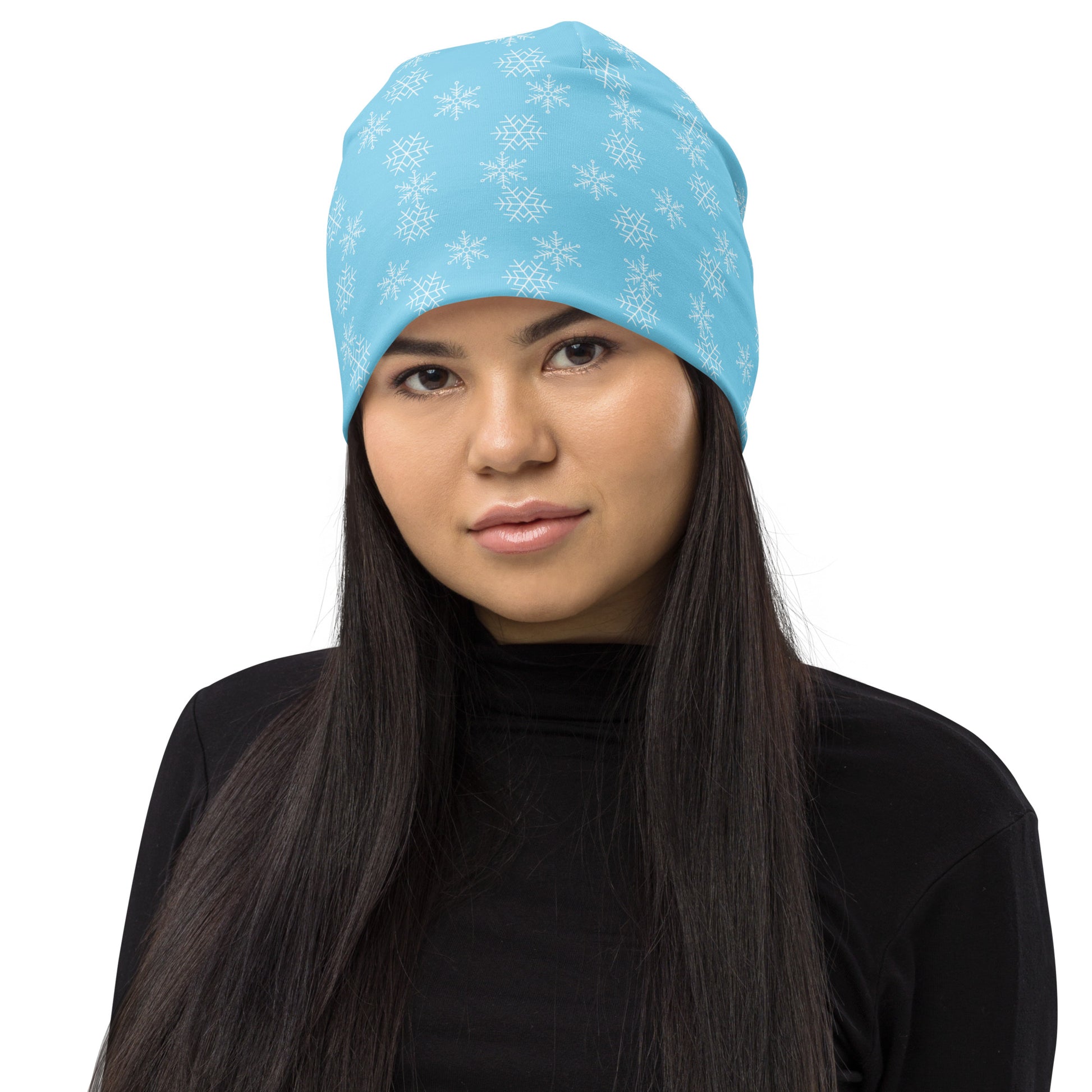 A person with long dark hair wearing a Snowflakes Beanie by Blue Sky Runners, featuring a stylish light blue hue adorned with white snowflakes, paired with a black turtleneck. The double-layered design of the beanie stands out beautifully against the plain white background.