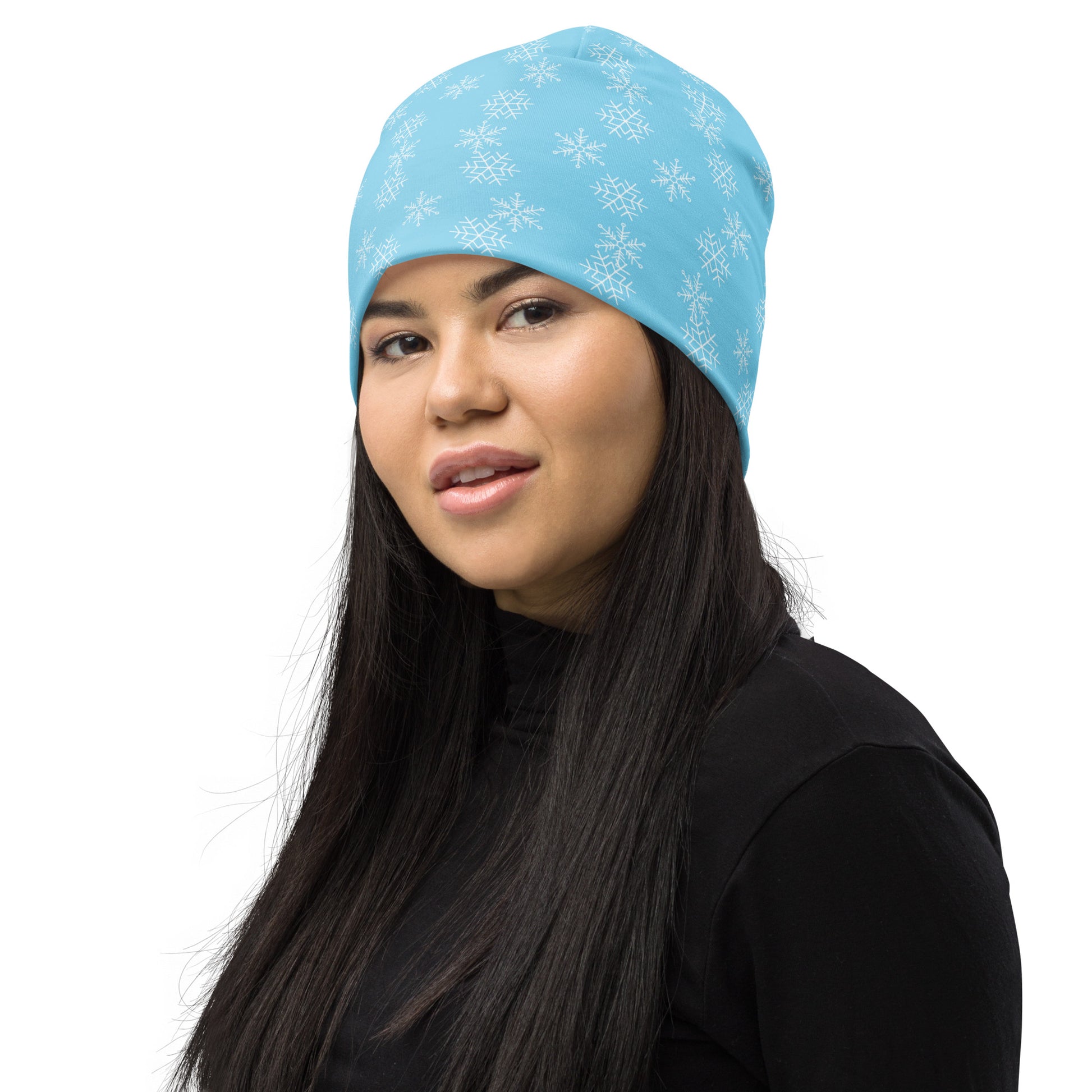 A person with long dark hair is wearing the Snowflakes Beanie from Blue Sky Runners—a stylish light blue hat featuring white snowflake patterns—paired with a black turtleneck sweater against a white background.