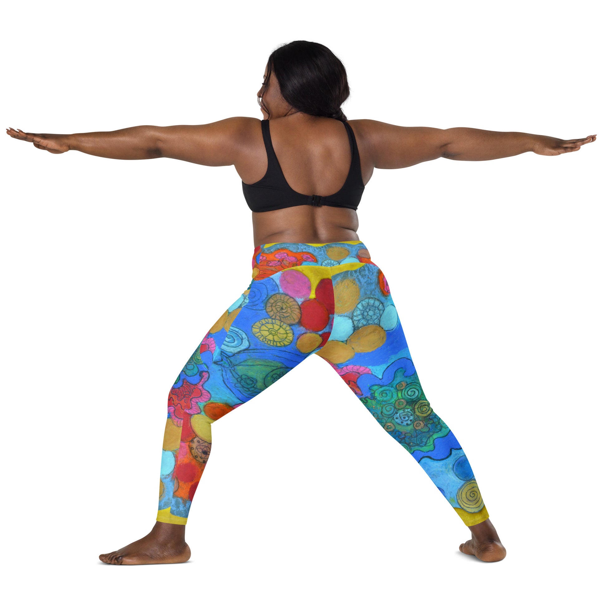 A woman performs a yoga pose with arms stretched out to the sides. She is wearing a black sports bra and vibrant, multicolored Coral leggings with pockets featuring abstract patterns by Blue Sky Runners. She stands on a non-descript background, likely a studio setting.
