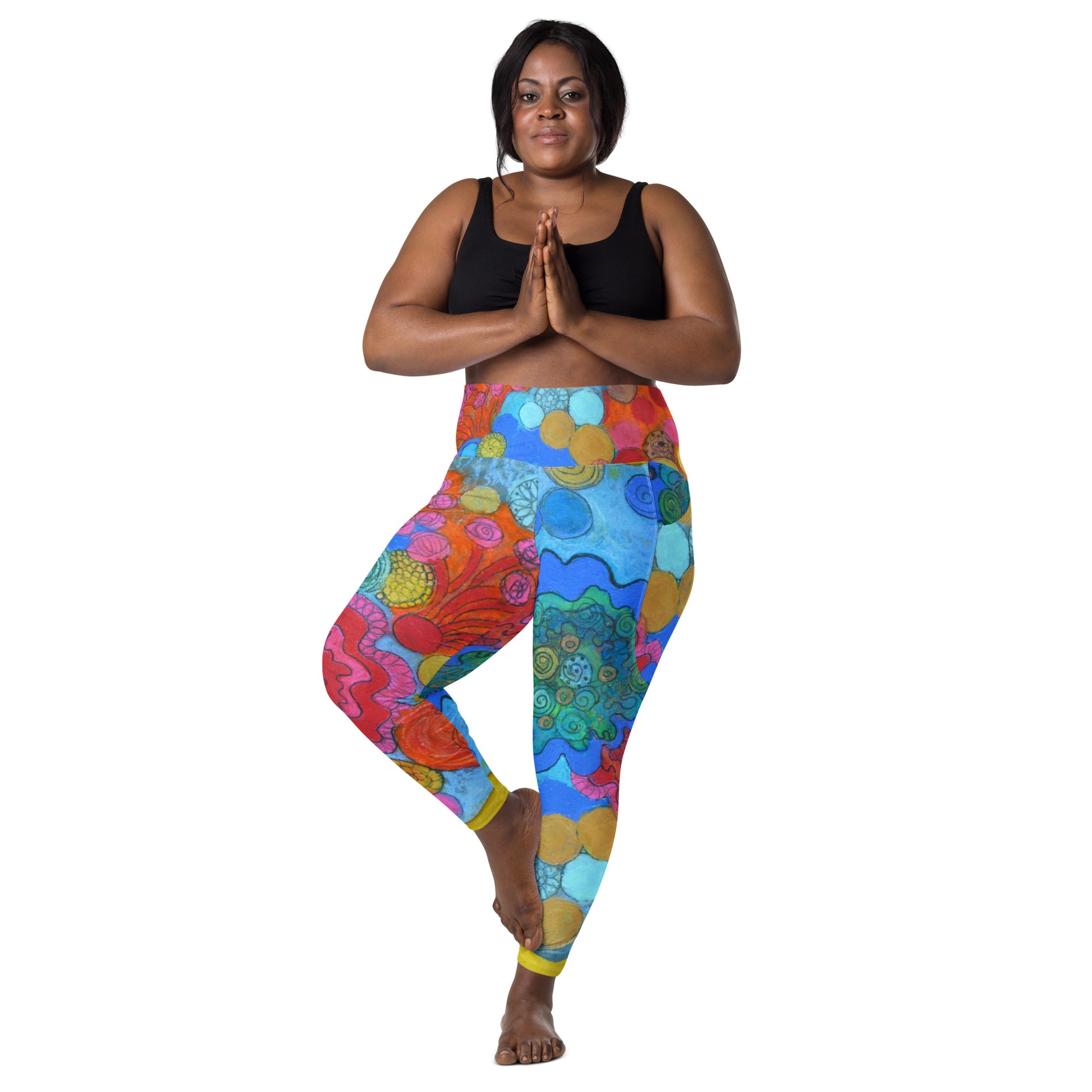 A woman stands in a yoga pose on one leg, wearing a black sports bra and the Coral - Leggings with pockets from Blue Sky Runners. She has her hands clasped together in front of her chest and smiles at the camera. The background is plain white.