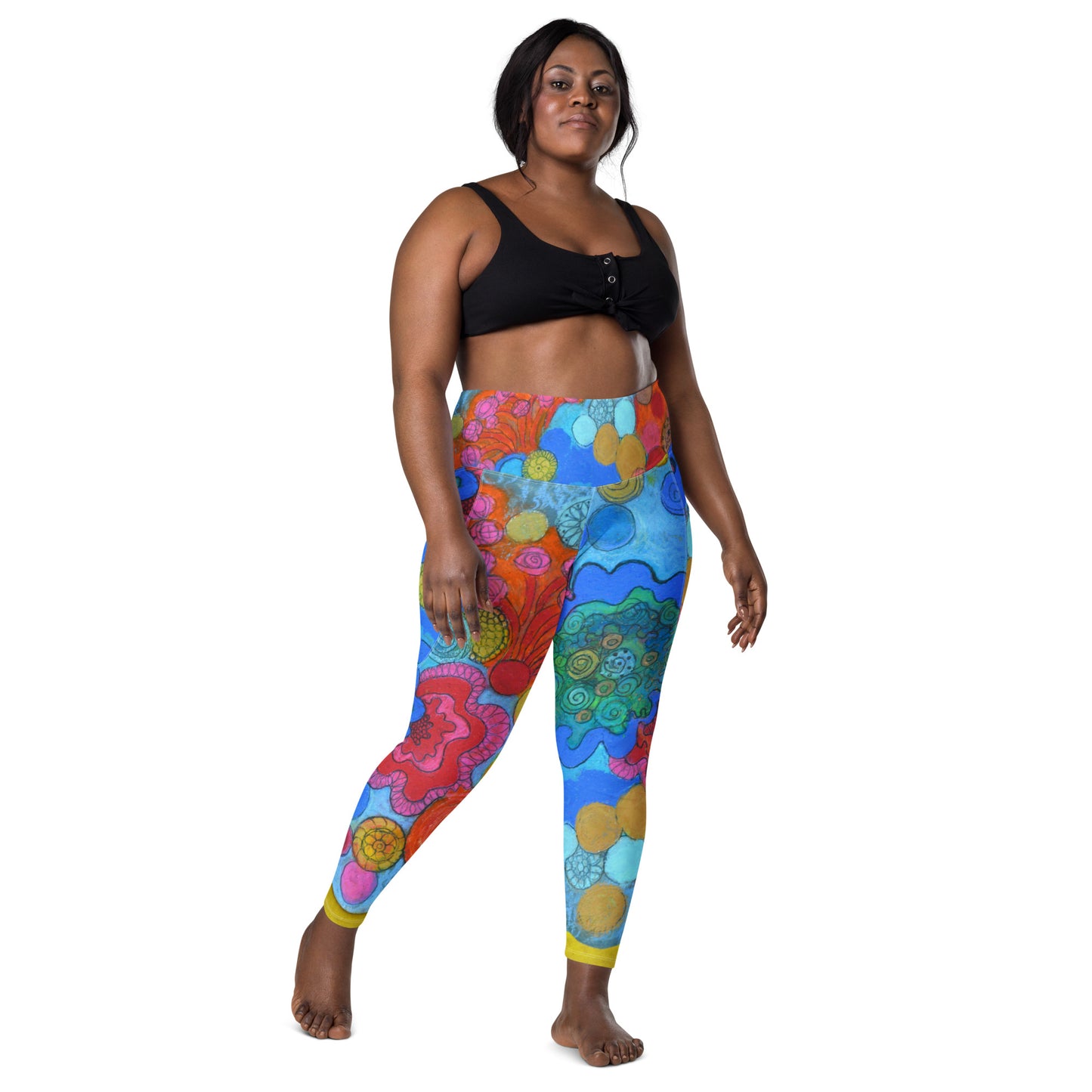 A person stands confidently wearing a black cropped top and the "Coral - Leggings with pockets" by Blue Sky Runners, featuring abstract, vibrant designs. They have a relaxed pose with one foot slightly forward and a calm expression, set against a plain white background.