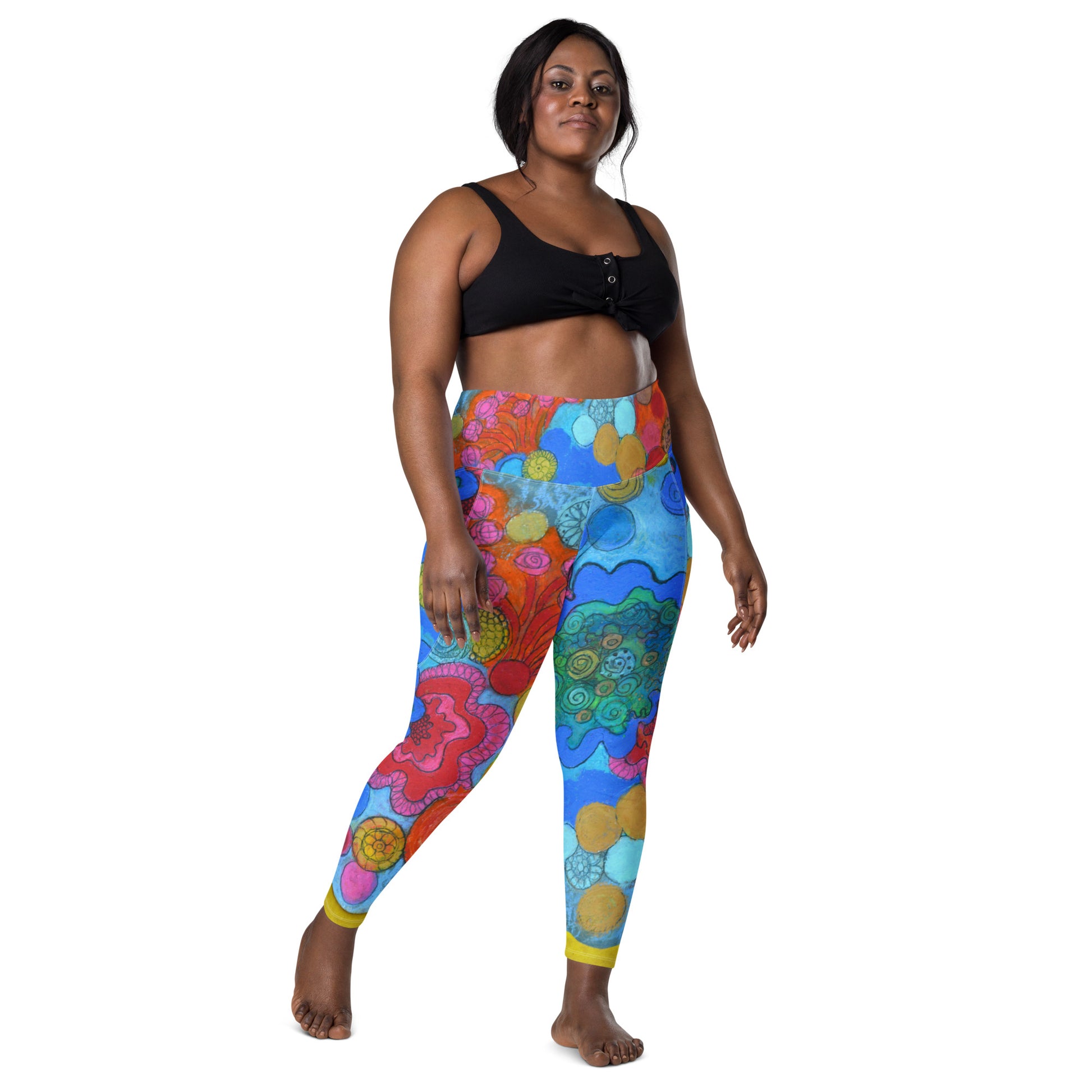 A person stands confidently wearing a black cropped top and the "Coral - Leggings with pockets" by Blue Sky Runners, featuring abstract, vibrant designs. They have a relaxed pose with one foot slightly forward and a calm expression, set against a plain white background.