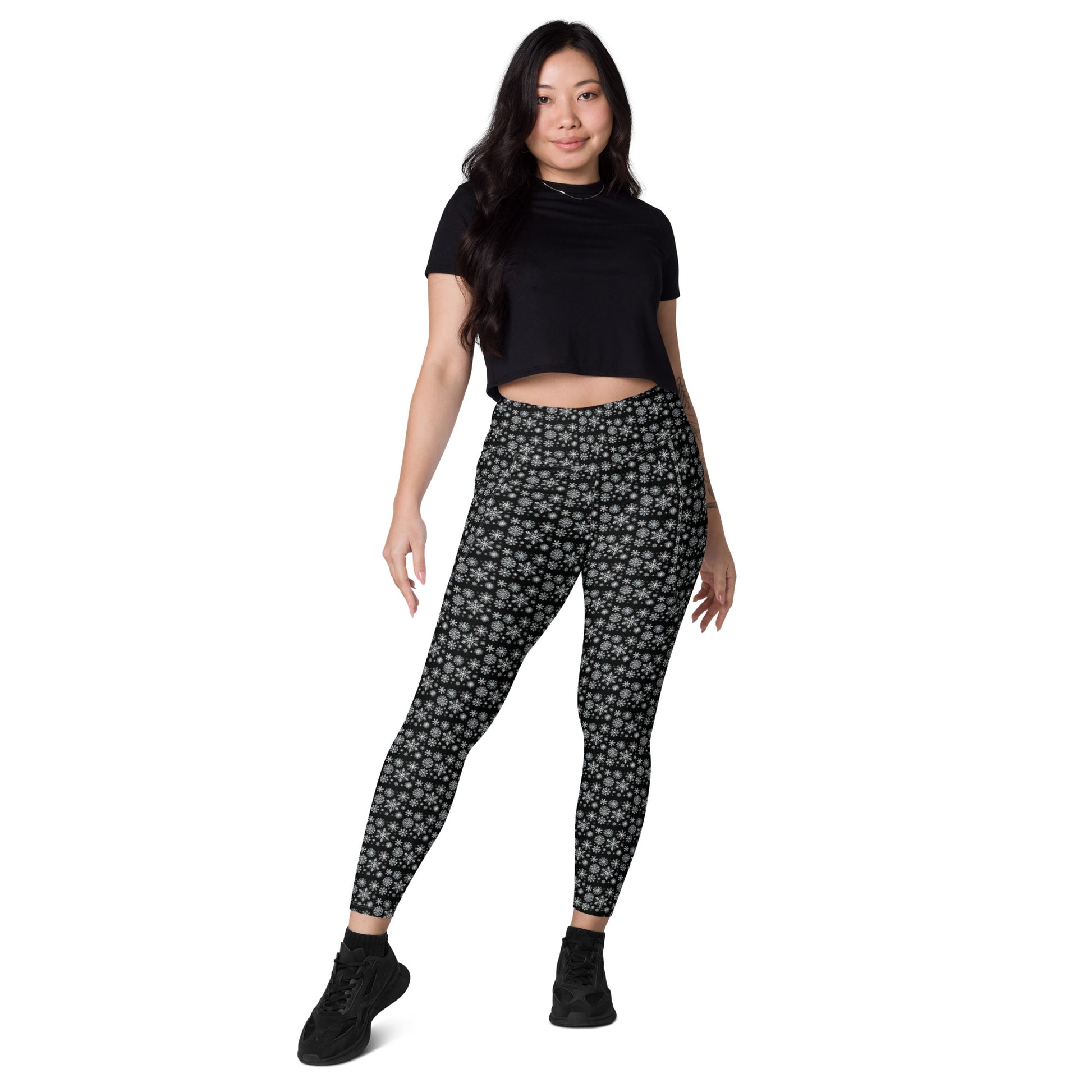 A person stands confidently wearing a black t-shirt and stylish Snowflakes Leggings with pockets from Blue Sky Runners. They have long dark hair and are sporting black sneakers, posing against a plain white background.