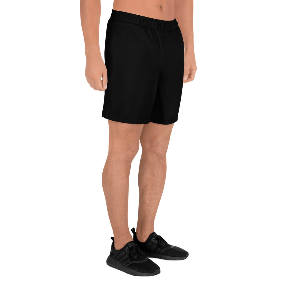 A person wearing Blue Sky Runners Men's Recycled Athletic Shorts in black, made of moisture-wicking fabric, and black athletic shoes is standing against a white background. The upper part of the body is not visible. The knee-length shorts and lace-up shoes feature a textured design, perfect for active use.