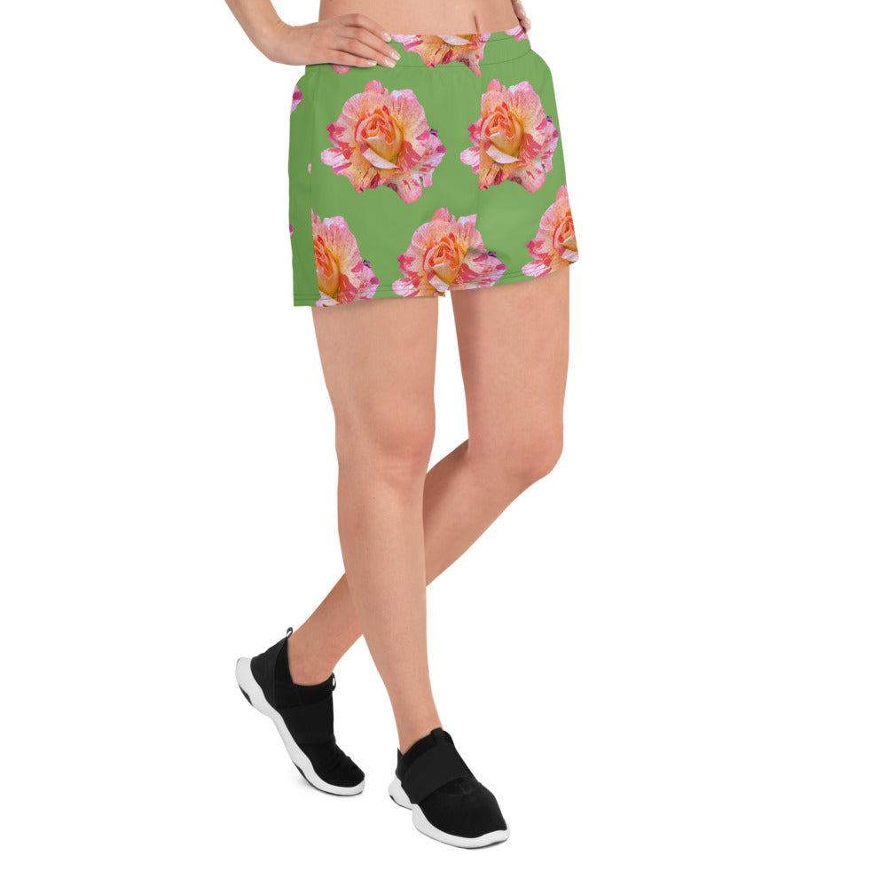 A person is wearing the Blue Sky Runners Roses BIG Roses on Green Women’s Recycled Athletic Shorts, which feature a vibrant pattern of large pink and yellow roses set against a green background. They are also wearing black sneakers. The focus is on the shorts and legs, highlighting a stylish and eco-friendly floral design.