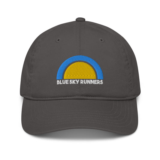 Presenting the Blue Sky Runners - Organic Hat from Blue Sky Runners, in a stylish dark grey. Crafted from eco-friendly organic cotton, this hat features a distinctive logo of a yellow half-circle beneath a blue arc, reminiscent of a sunrise. The words "BLUE SKY RUNNERS" are elegantly embroidered in white below the logo. Designed with a curved brim and an adjustable back for comfort and fit.
